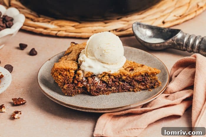 A plate with a slice of brown butter pecan chocolate chip skillet cookie and a scoop of ice cream.