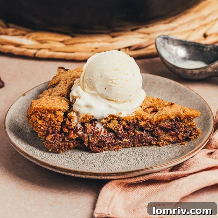 A plate with a slice of brown butter pecan chocolate chip skillet cookie and a scoop of ice cream.