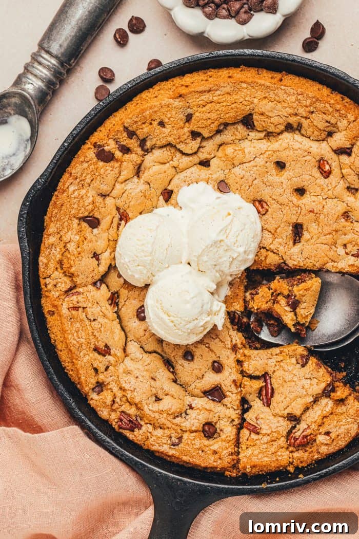 An image of the whole chocolate chip cookie skillet with two slices removed and a few scoops of ice cream in the middle.