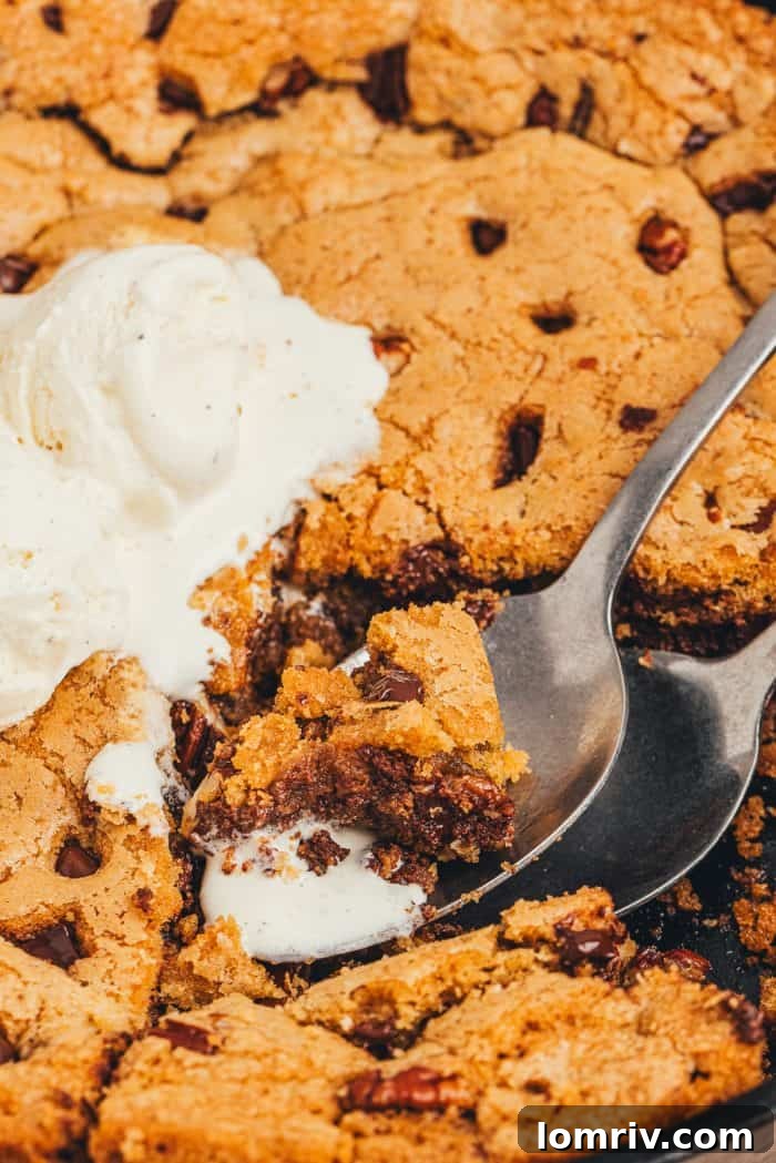 A spoon with a bite of chocolate chip cookie skillet and melted ice cream.