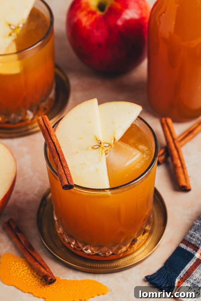 A glass with an Apple Cider Old Fashioned and garnished with two apple slices and a cinnamon stick, perfectly capturing the essence of fall.