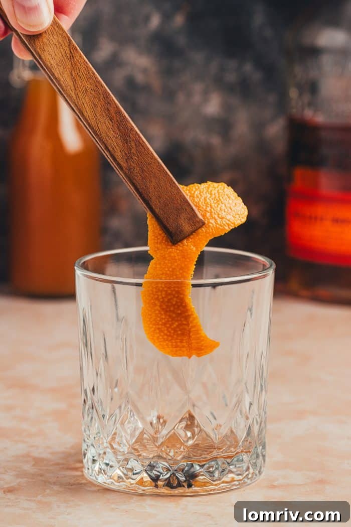 A strip of orange peel being added to an Old Fashioned glass, ready for muddling.
