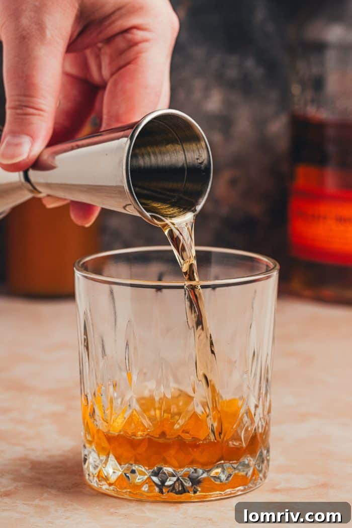Bourbon being poured into a glass containing the muddled orange peel, bitters, and simple syrup.