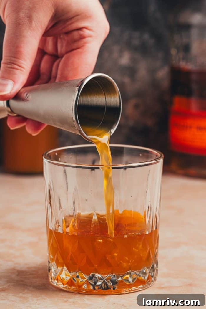 The final step: pouring apple cider into the glass with bourbon and other ingredients, completing the cocktail.