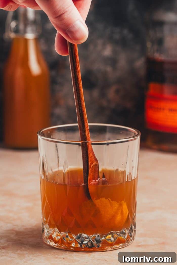 A bar spoon stirring the Apple Cider Old Fashioned, ensuring all ingredients are well combined.