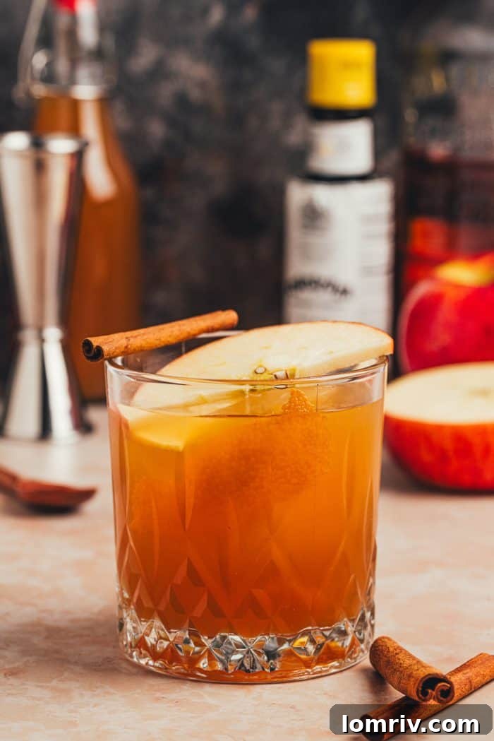 The finished Apple Cider Old Fashioned cocktail, elegantly presented with bottles in the background, ready for enjoyment.