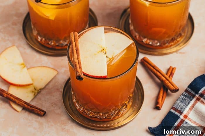 Three glasses of Apple Cider Old Fashioned, each garnished meticulously with cinnamon sticks and apple slices, a perfect spread for a fall celebration.