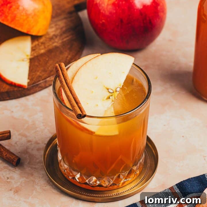 A glass of Apple Cider Old Fashioned with cinnamon sticks and apple slices.