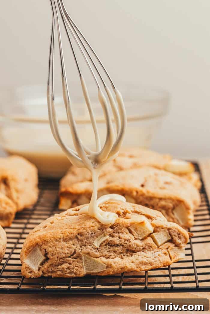 Apple cinnamon scones being drizzled with a maple glaze on a black wire rack.