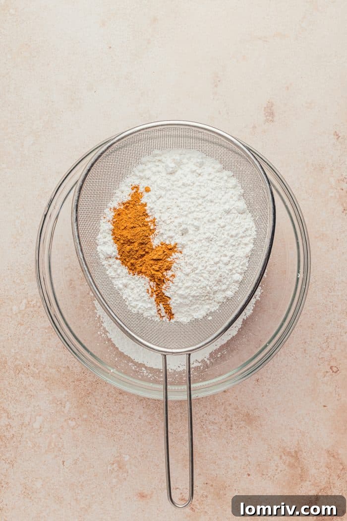 A glass bowl filled with dry ingredients: flour and cinnamon being expertly sifted.
