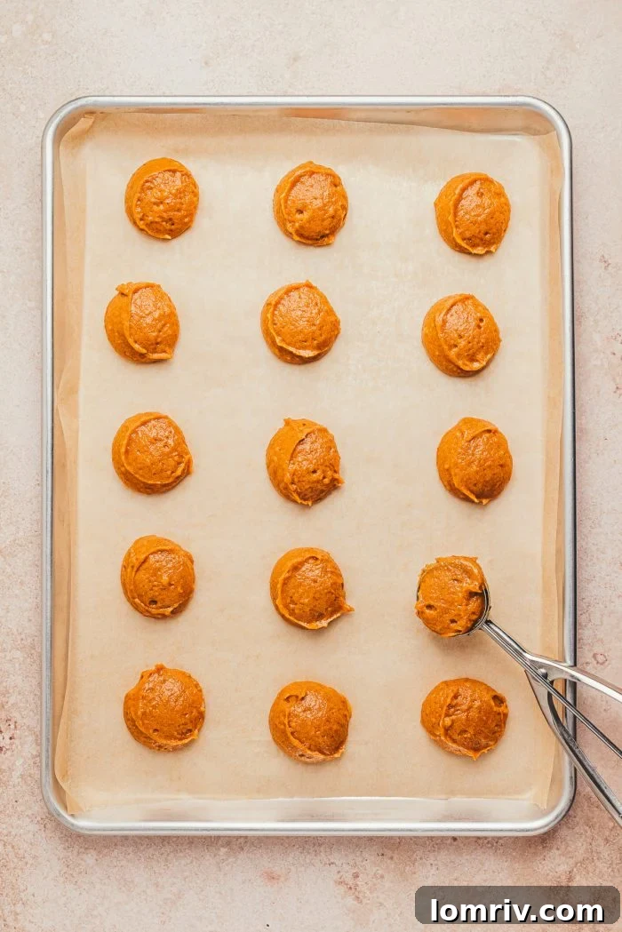 Rows of unbaked pumpkin whoopie pie batter neatly arranged on a parchment-lined baking sheet, ready for the oven.