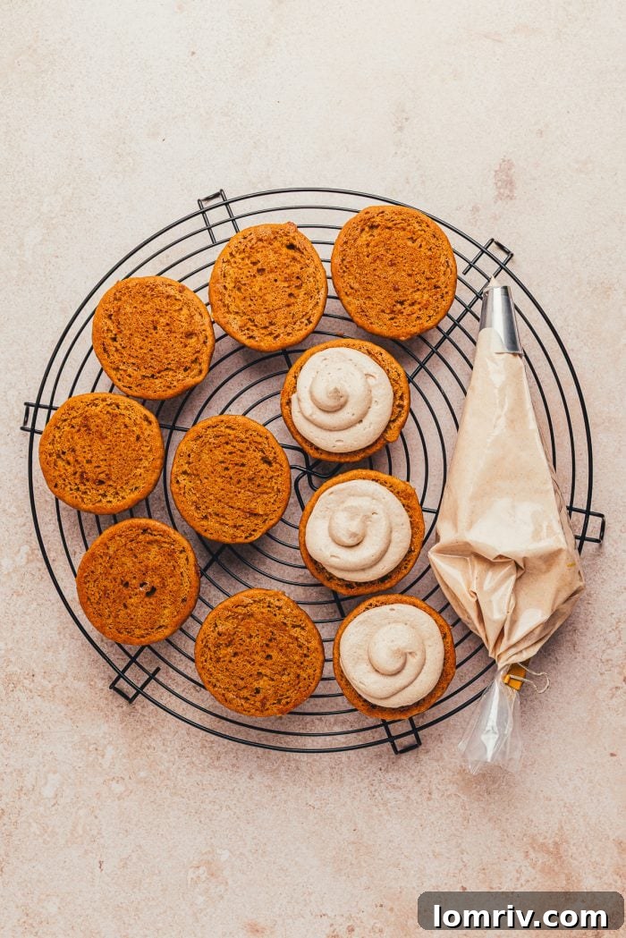 Halved pumpkin whoopie pies meticulously piped with creamy cinnamon cream cheese filling, ready to be sandwiched.