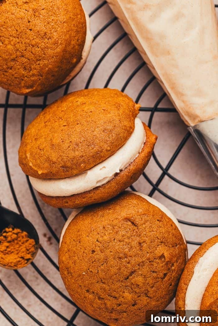 A collection of perfectly assembled pumpkin whoopie pies with cinnamon cream cheese filling, arranged on a cooling rack.
