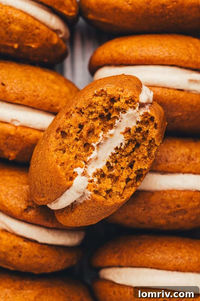 An inviting close-up of a pumpkin whoopie pie, revealing its creamy filling after a bite has been taken.