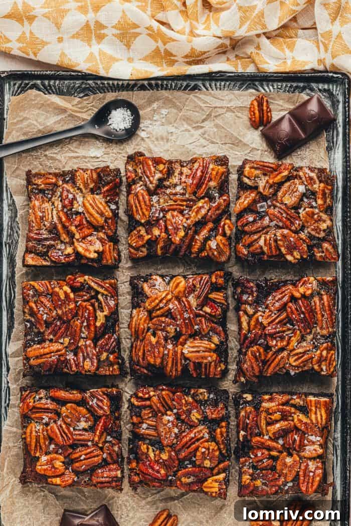 Brownies with a pecan pie topping are sliced and displayed on parchment paper.
