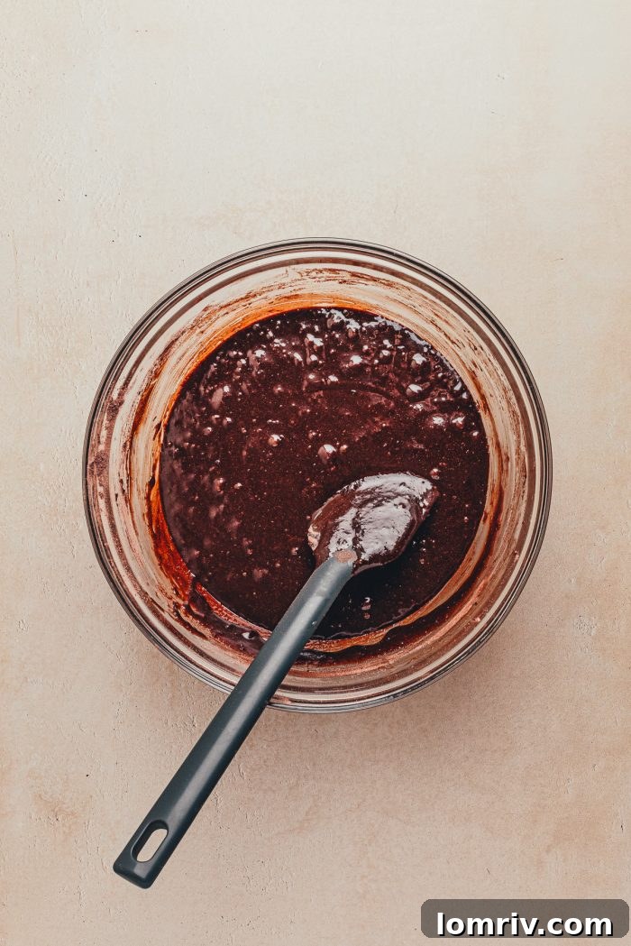 The sugar and flour mixture added to the melted chocolate mixture in a glass bowl.