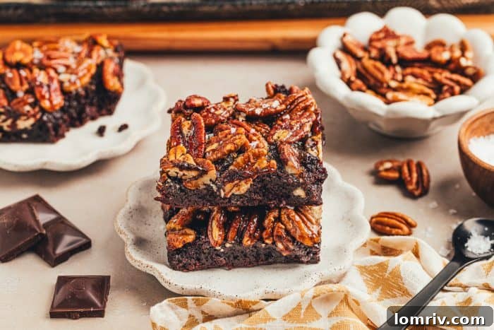 A brownie with a pecan pie topping is on a white plate with pecans scattered around it.