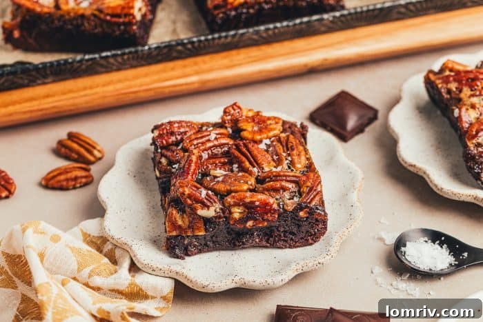 A brownie with a pecan pie topping is on a white plate with pecans scattered around it.