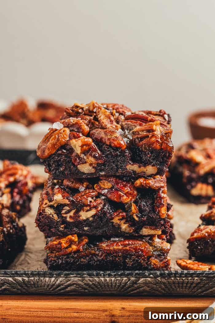 A stack of 3 brownies with pecan pie topping with various brownies in the background.