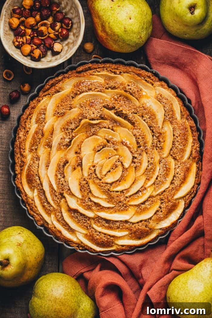 An inviting overhead shot of a golden hazelnut frangipane pear tart, nestled on a rustic wooden surface with a soft red napkin draped alongside.