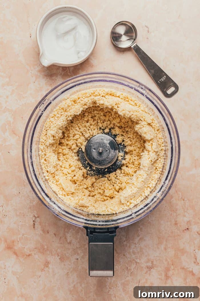 The crumbly tart dough mixture, starting to come together, is visible in the food processor bowl.
