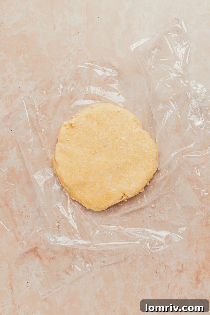 A disc of chilled tart dough, wrapped in plastic, ready to be rolled out, on a clean surface.