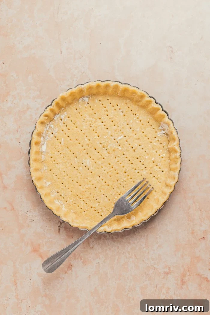 A fork is used to prick the unbaked tart shell crust, preparing it for blind baking to prevent bubbling.