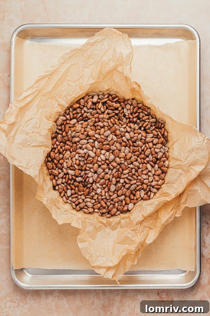 Dried beans, acting as pie weights, are shown covering the parchment paper inside the unbaked tart crust, ready for blind baking.