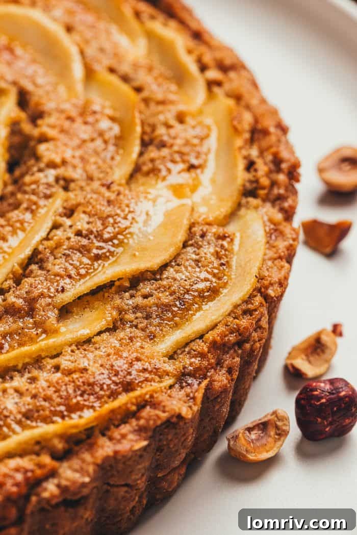 A close-up view revealing the rich, golden-brown hazelnut frangipane filling beneath a layer of perfectly arranged pear slices in a baked tart.