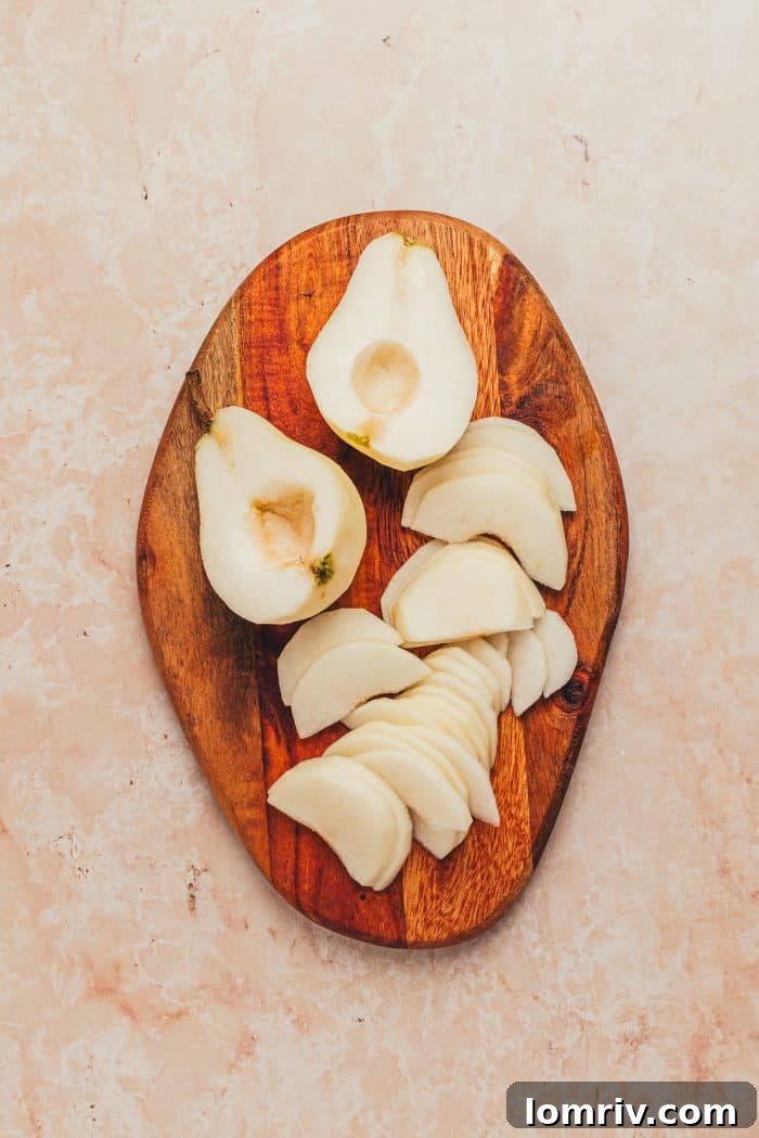 A collection of thinly sliced pears, fanned out on a wooden cutting board, ready for arrangement on the tart.