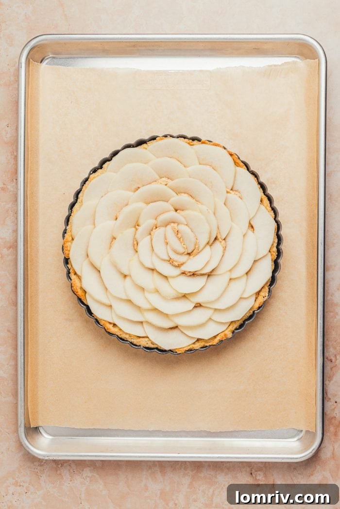 Artfully arranged pear slices cover the frangipane filling within the tart shell, forming a beautiful pattern.