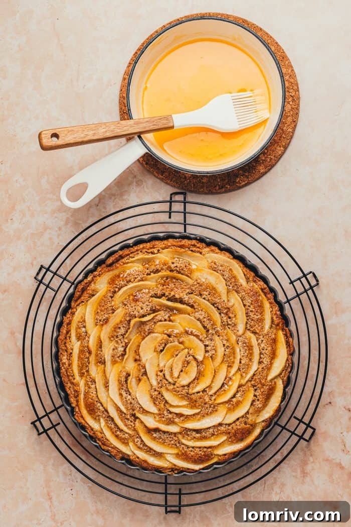 Warm apricot jam, thinned in a saucepan, is being carefully brushed over the pear slices of the freshly baked tart.