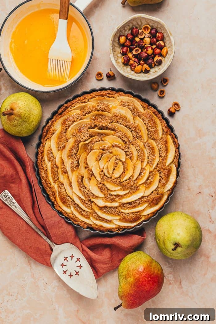 The exquisite finished hazelnut frangipane pear tart, now glazed and glistening, photographed from above with a red napkin beside it.