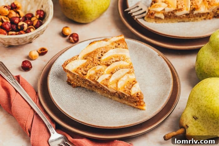 A perfectly presented slice of pear tart on two white plates, with fresh pears artfully blurred in the background, creating a rustic feel.