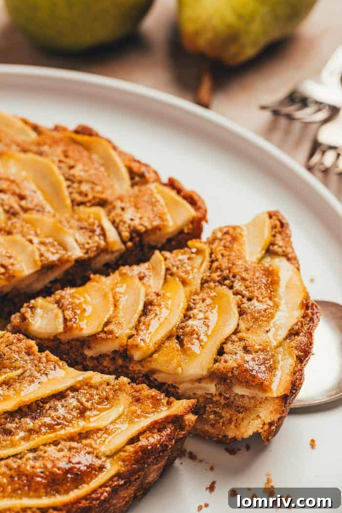 An overhead shot capturing a hand gently lifting a slice of pear frangipane tart from the pan, revealing the delicate layers.