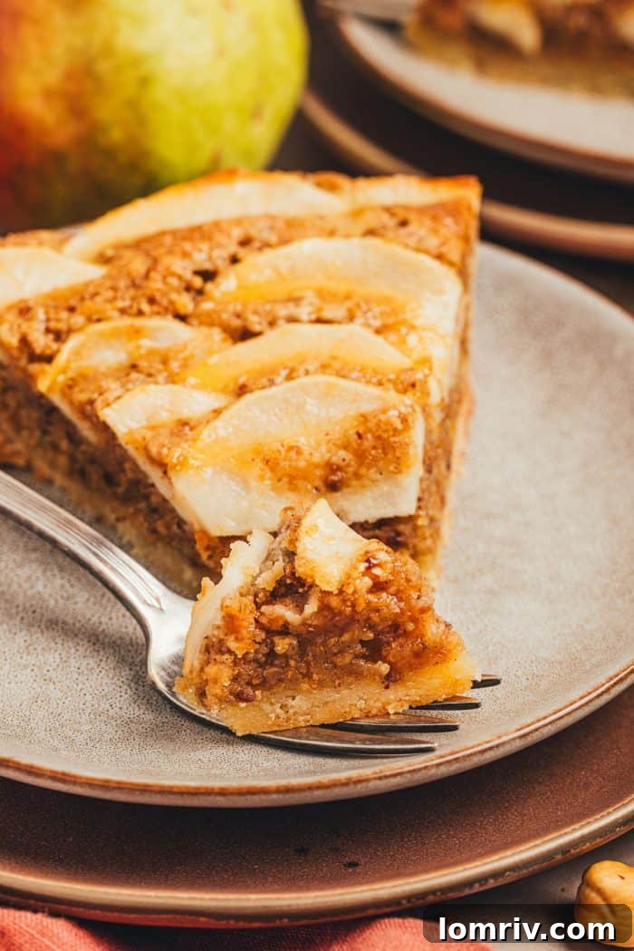 A mouth-watering slice of pear frangipane tart on a white plate, with a bite taken, showcasing the crisp crust, rich filling, and soft pears.