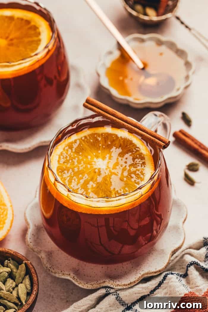 A glass mug filled with chai vanilla bean hot toddy and garnished with orange slices, radiating warmth.