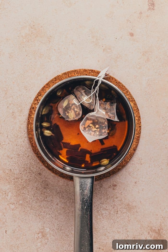 Chai tea bags steeping in a saucepan with spices and orange peel, creating a fragrant base for the hot toddy.
