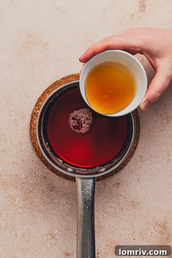 Golden honey being poured into the simmering chai hot toddy mixture in a saucepan, adding natural sweetness.