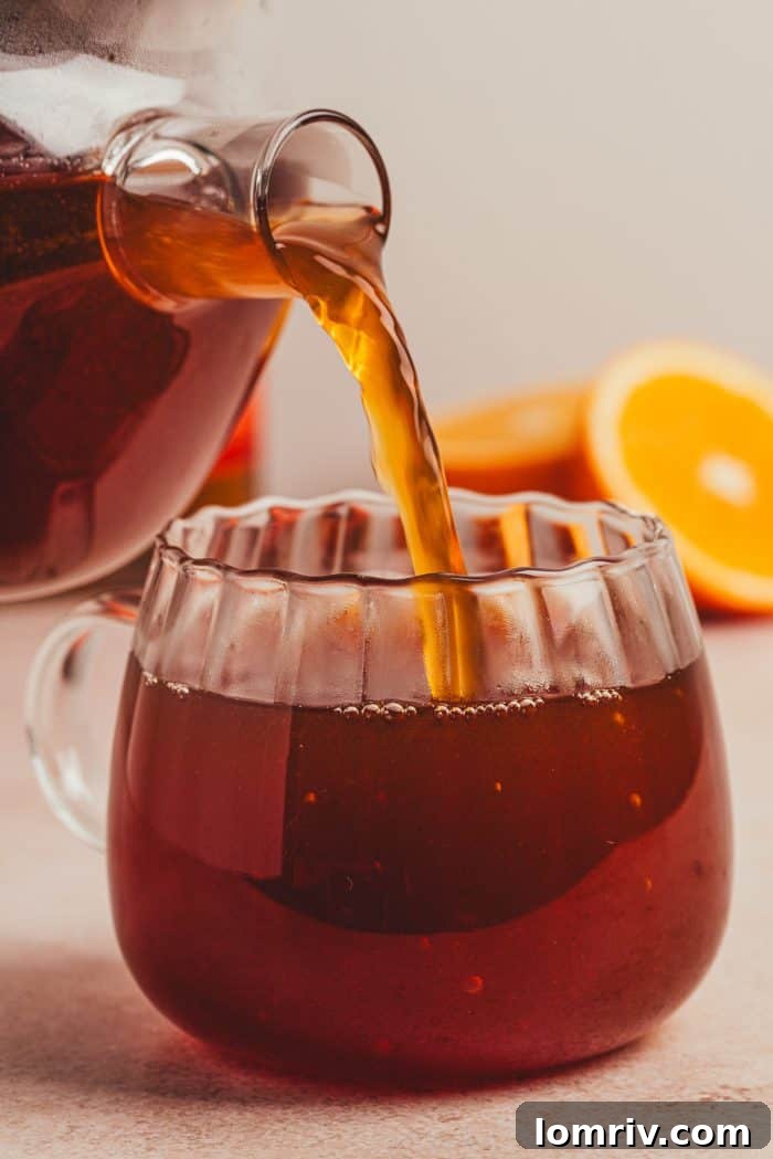 The spiced chai hot toddy mixture being carefully poured from a saucepan into a waiting glass mug.