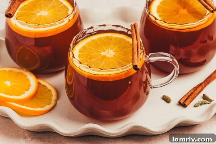 A trio of chai hot toddies, each perfectly garnished with orange slices and cinnamon sticks, arranged for a comforting gathering.