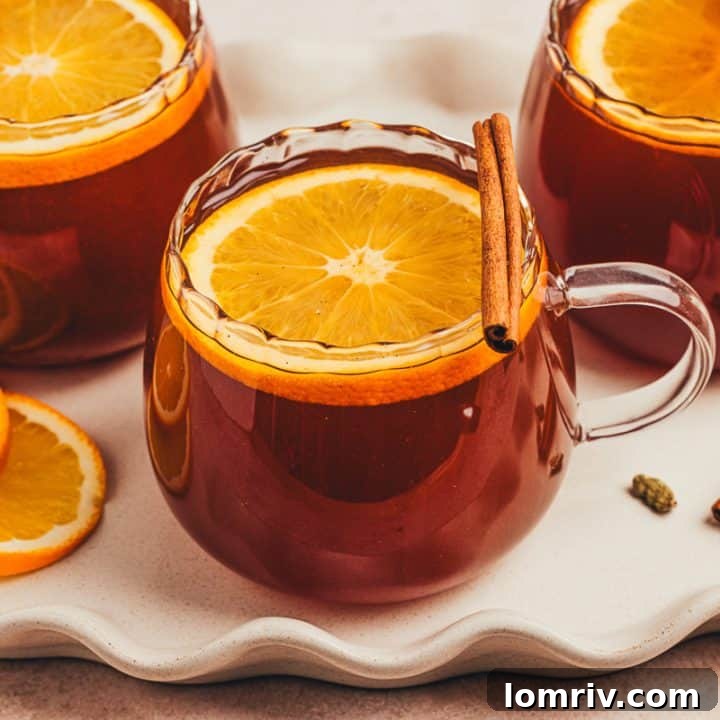 A collection of three chai vanilla bean hot toddies, adorned with orange slices and cinnamon sticks, presented in glass mugs.