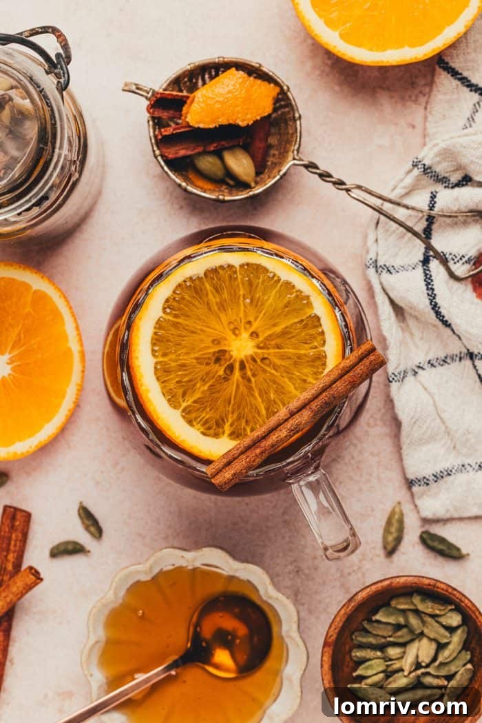 A glass mug filled with chai vanilla bean hot toddy, garnished with a vibrant orange slice and a cinnamon stick, ready to be enjoyed.