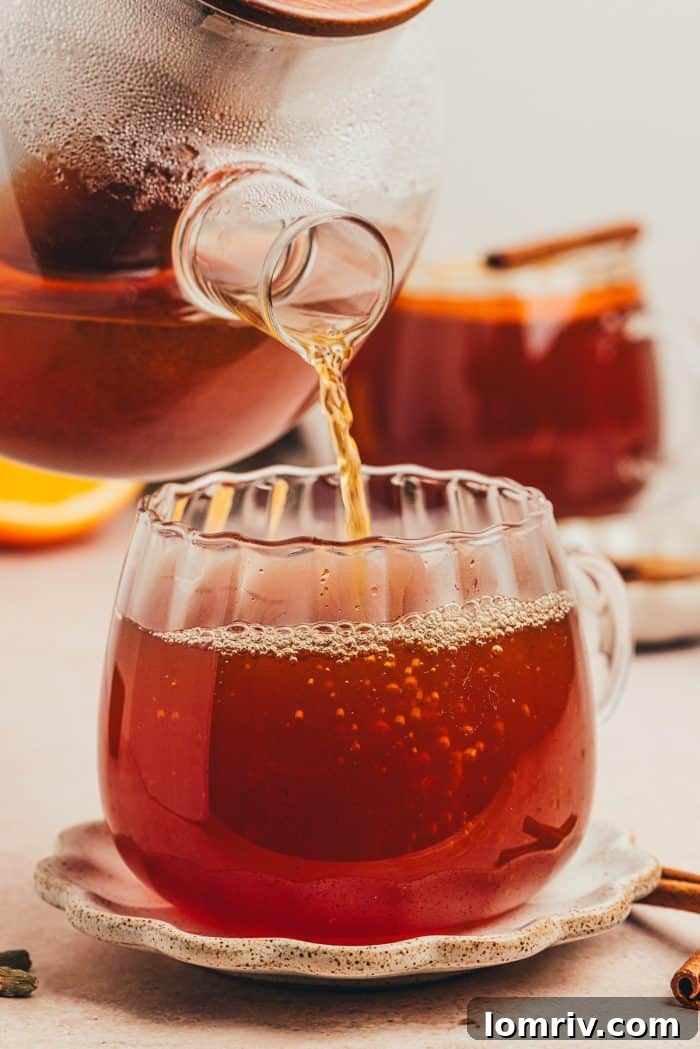 The golden-hued hot toddy being poured from a saucepan into an elegant glass mug, steam gently rising.