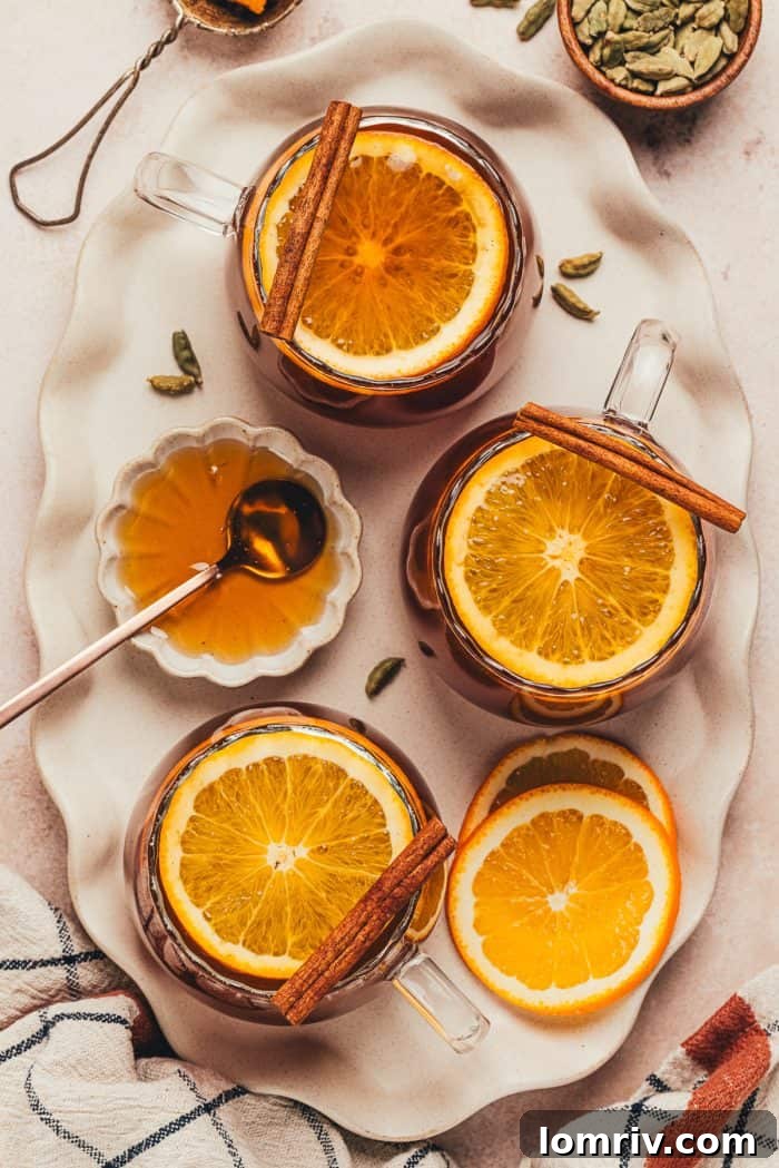 Two glass mugs, perfectly garnished with orange slices and cinnamon sticks, filled with the inviting chai vanilla bean hot toddy.