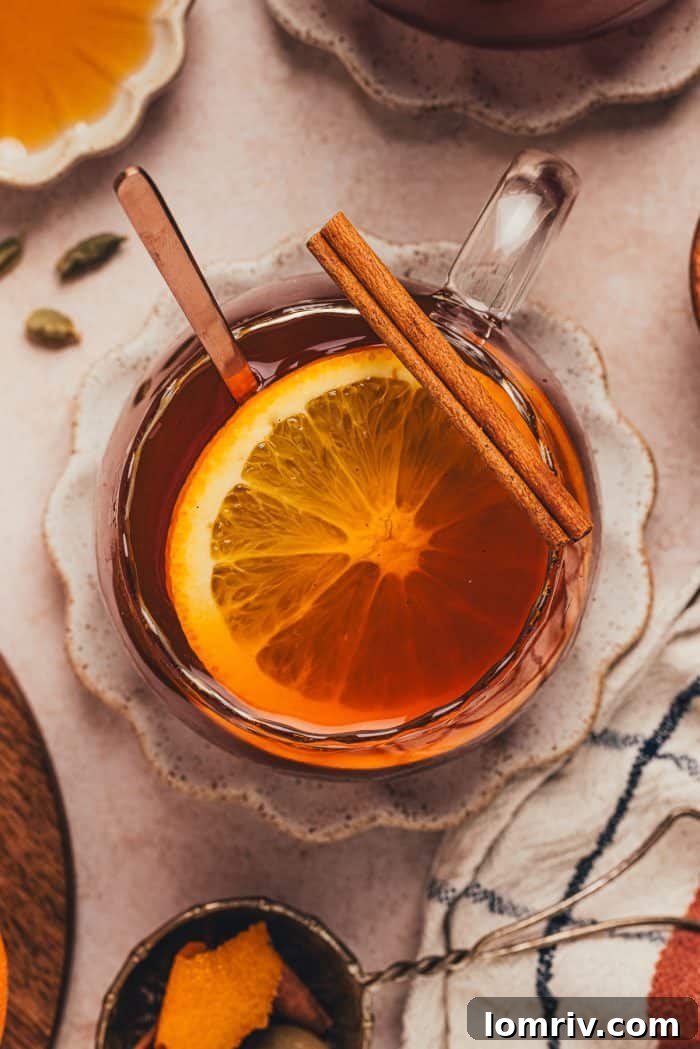 A close-up shot of a glass mug of chai vanilla bean hot toddy, adorned with orange slices, inviting a comforting sip.