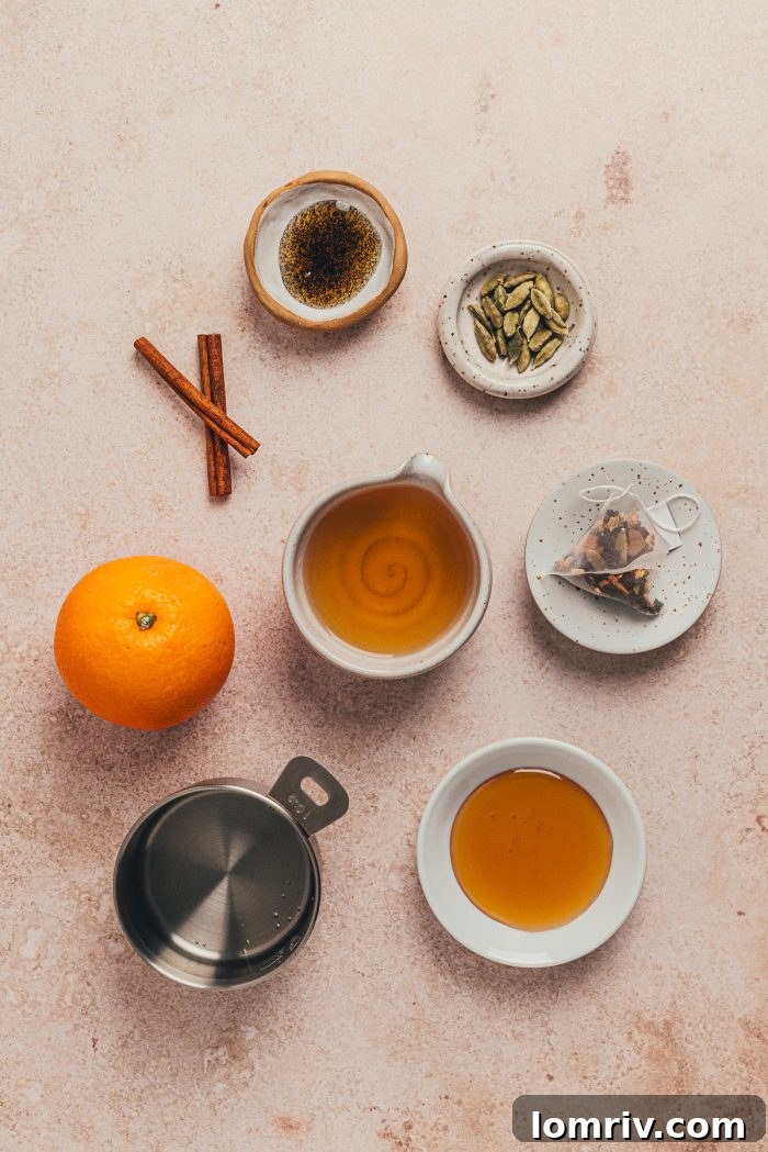 An array of ingredients for a Chai Hot Toddy, including whole spices, honey, and oranges, thoughtfully arranged in bowls.