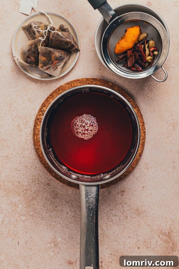Water, cinnamon sticks, cardamom pods, and orange peel gently simmering in a saucepan for the hot toddy base.