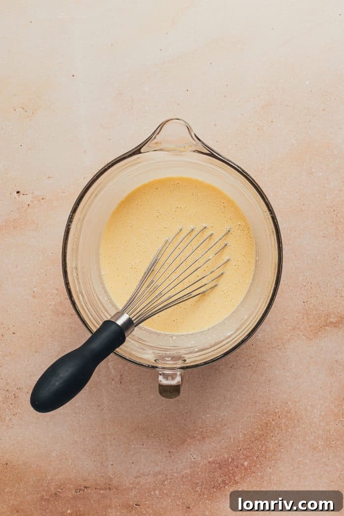 The popover batter in a large sprouted mixing bowl with a whisk.