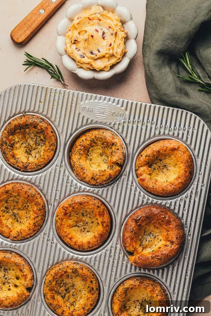 Herbed popovers in a baking tray with a green napkin and a bowl of butter in the background.
